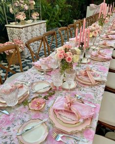 the table is set with pink and white plates, silverware, and flowers in vases