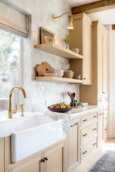 a white kitchen sink sitting under a window next to a wooden shelf filled with fruit