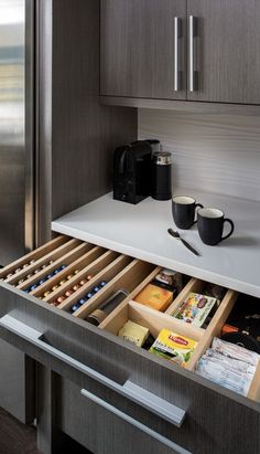 an open drawer in a kitchen next to a refrigerator and coffee mug on the counter