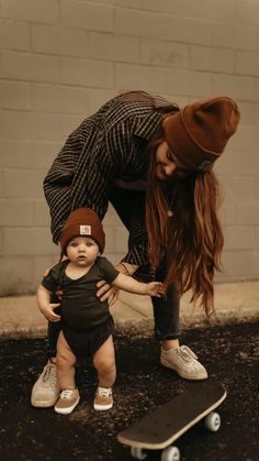 a woman bending over next to a baby on top of a skateboard while wearing a hat