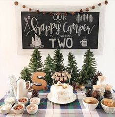 a table topped with lots of food next to a chalkboard sign that says happy camper is turning two