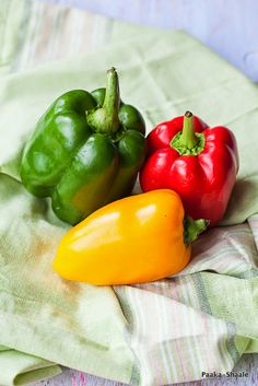 three different colored peppers sitting on top of a green cloth next to each other,