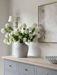 a vase with white flowers sitting on top of a dresser