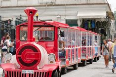 a red and white train is on the street with people walking around in front of it