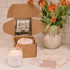 a candle and some flowers on a white table with a brown box in the middle