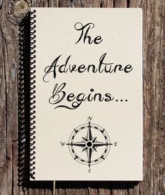 a notebook with the words the adventure begins written on it next to a wooden background