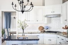 a chandelier hangs from the ceiling in a kitchen with white cabinets and granite counter tops