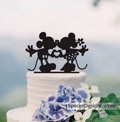 a wedding cake topper with mickey and minnie kissing on it's head, surrounded by blue flowers