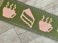 a knitted table runner with coffee cups and toasters on it, sitting on a wooden floor