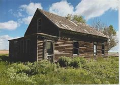 an old run down wooden house in the middle of a grassy field with blue sky and clouds