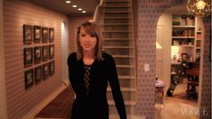 a woman is standing in the middle of a room with stairs and pictures on the walls