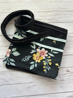 a black and yellow flowered purse sitting on top of a white wooden floor next to a black strap