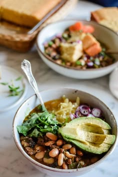 two bowls filled with beans, avocado and other foods on top of a table