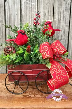 a wagon filled with red flowers and greenery sitting on top of a wooden table