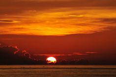 the sun is setting over the ocean with clouds