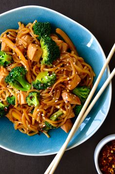 a blue bowl filled with noodles and broccoli next to chopsticks on a table