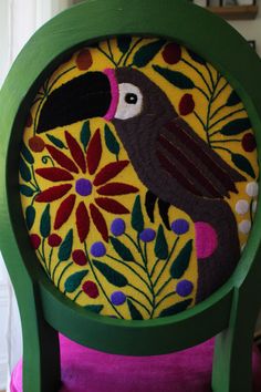 a green chair with a colorful bird painted on it's back and seat cushion