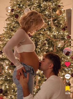 a man kneeling next to a woman in front of a christmas tree