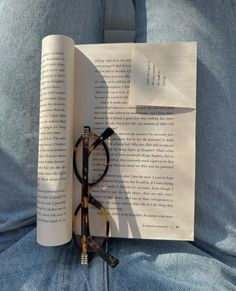 an open book with reading glasses on it sitting on someone's lap, next to a pair of reading glasses