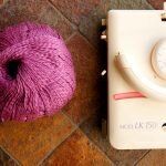 a pink ball of yarn sitting next to a white sewing machine on a tile floor