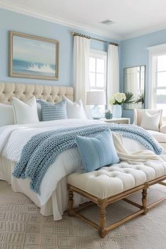 a bedroom with blue walls, white bedding and an ottoman in front of the bed