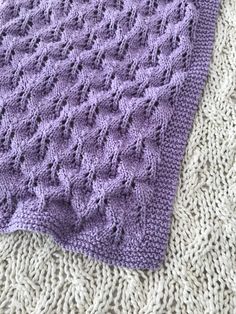 a purple crocheted blanket laying on top of a white knitted floor mat