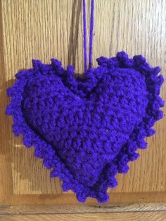 a purple crocheted heart hanging on a wooden door with string attached to it