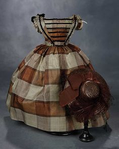 an old fashion dress and hat is displayed on a stand with a gray background in the foreground