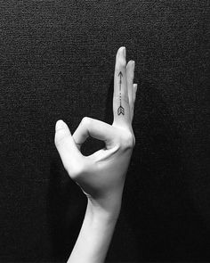 a person's hand with a tattoo on it holding up the peace sign in front of a black background