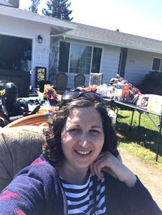 a woman sitting in front of a house with lots of stuff on the lawn behind her