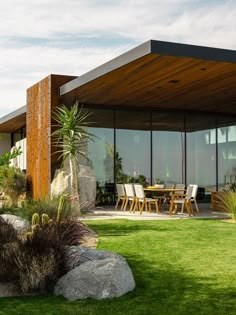 an outdoor dining area with grass, rocks and plants in front of a modern house