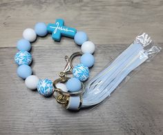 a blue and white beaded bracelet with a cross charm on the end, sitting on a wooden table