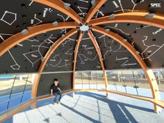 a man sitting on top of a wooden bench under a roof covered in stars and constellations