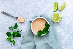 a bowl of sauce with cilantro and limes next to it on a blue towel