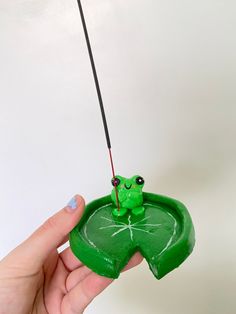 a hand holding a green frog toy with a fishing rod in it's mouth