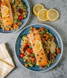 two plates with salmon, rice and vegetables on them next to lemon wedged slices