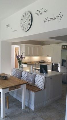 a kitchen with a wooden table and bench next to a wall clock on the wall