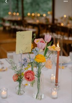 flowers in vases on a table with candles and note pinned to the wall behind them