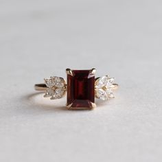 Metal: 14K Yellow Gold Stone: Emerald Cut Garnet  Stone Weight: 1.5 carat Stone Size: 5.75mm x 7.79mm Accent Stones: Natural Diamonds Accent Shapes: Marquise  Shank: 1.6mm Garnet Rings Vintage, Elegant Red Ruby Cluster Ring, Elegant Red Cluster Diamond Ring, Luxury Cluster Ruby Ring Gift, Garnet Diamond Ring With Prong Setting, Fine Jewelry Garnet Diamond Ring With Prong Setting, Luxury Red Cluster Promise Ring, Elegant Garnet Cluster Ring For Anniversary, Elegant 14k Gold Cluster Ruby Ring