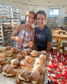 two women standing next to each other in front of trays of pastries and desserts