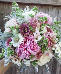 a bridal bouquet with pink, white and green flowers in front of a wooden fence