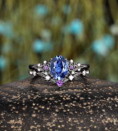 a ring with an oval blue stone surrounded by pink and white stones on top of a rock