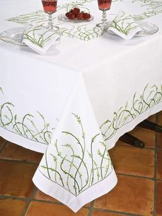 the table is covered with white linens and has green designs on it, along with two wine glasses