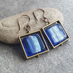 These pretty brass square earrings are made from square bead frames in antique brass colour, into which I've wired a pair of lovely cornflower blue glass beads - they have a silver foil lining which looks amazing when the light shines through them. The earrings hang from handmade copper ear wires (sterling silver or gold plated available on request) and despite looking quite chunky, are comfortable to wear. The square bead earrings would make a lovely piece of bohemian jewelry and an unusual 21st birthday gift! A matching pendant and bracelet are also available as shown in the last two photos. Find them separately in my shop here: www.etsy.com/uk/listing/1746080372 and www.etsy.com/uk/listing/1760280055 Length: 4cm from top of ear wires. Beaded components are 2.5cm (1") side to side. Sent Square Metal Earrings For Gifts, Square Metal Earrings For Gift, Handmade Square Green Earrings, Blue Square Earrings For Gift, Handmade Multicolor Square Earrings, Blue Gemstone Square Pendant Jewelry, Bead Frames, Blue Jewellery, Blue Wire-wrapped Glass Earrings