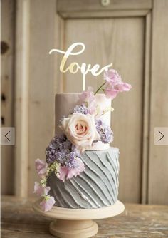 a wedding cake with flowers and the word love spelled on top is sitting on a table