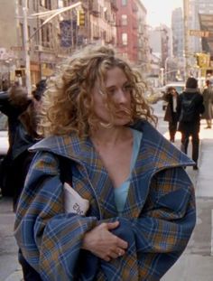 a woman with curly hair walking down the street wearing a blue and yellow plaid coat