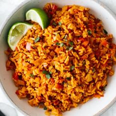 a white bowl filled with mexican rice and lime wedged in the corner next to it