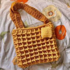 a crocheted purse sitting on top of a bed next to an orange flower