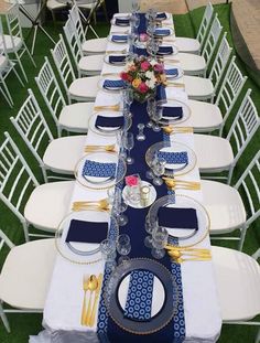 a long table set up with white chairs and blue runneres for an outdoor event