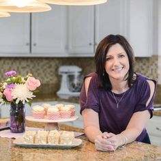 a woman sitting at a kitchen counter in front of a plate of cookies and flowers